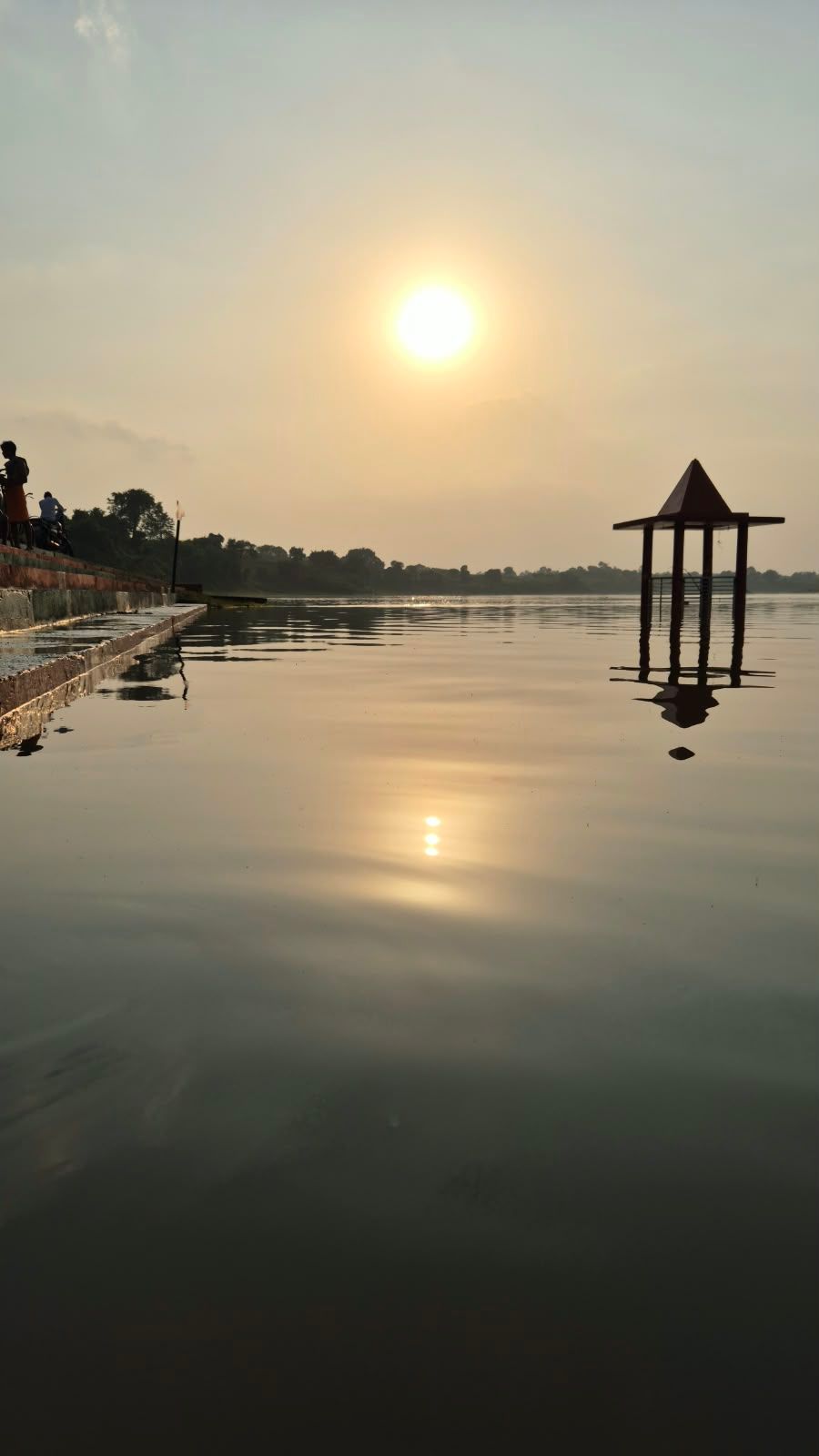 The sun setting over the Narmada, with a small temple standing half in the water